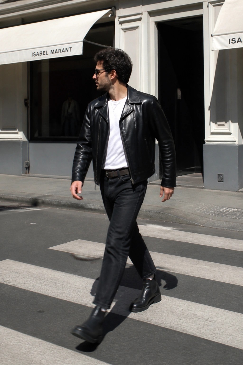 Man in black leather jacket crossing sunny city street on crosswalk