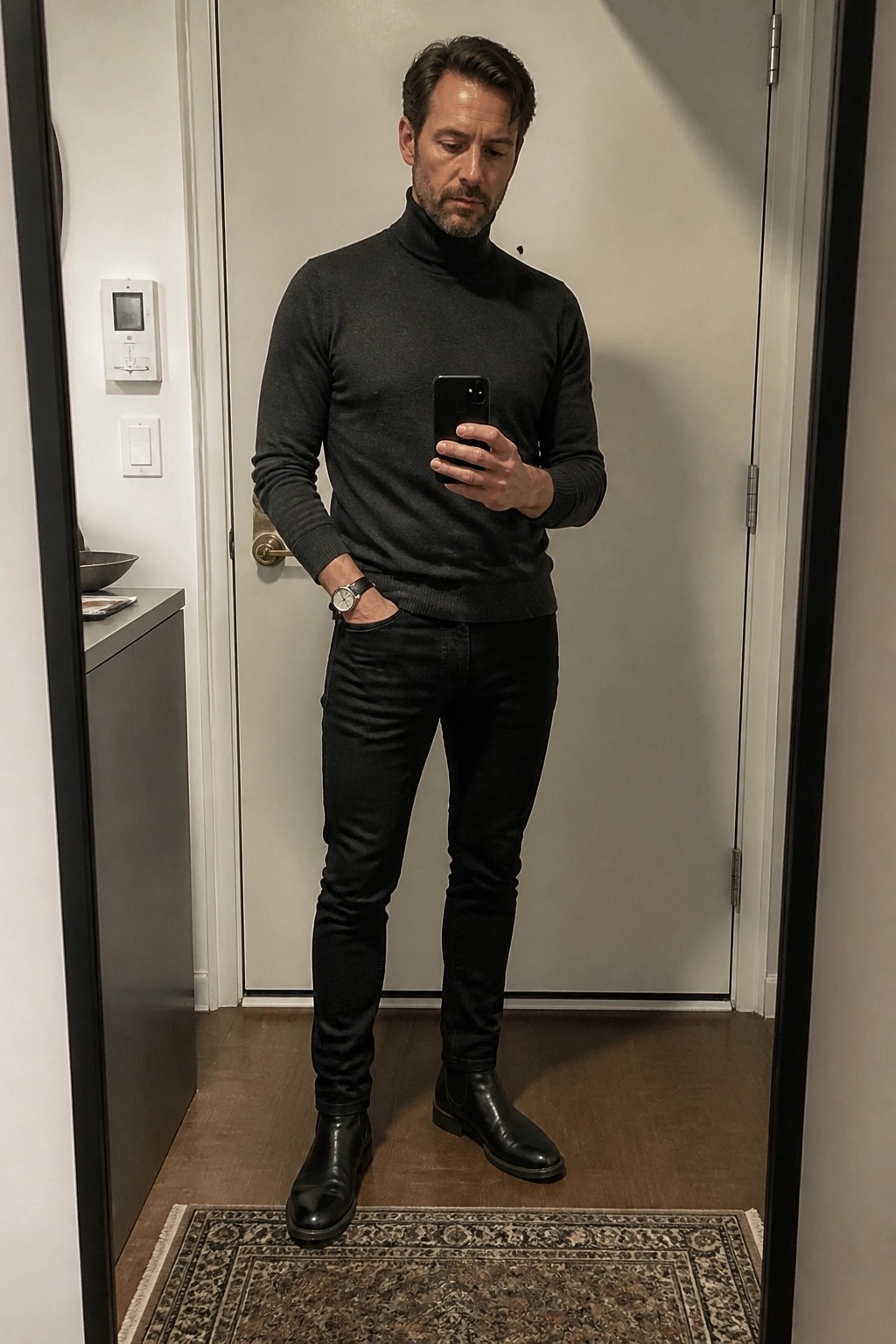 Man in gray turtleneck sweater and black jeans taking mirror selfie with phone
