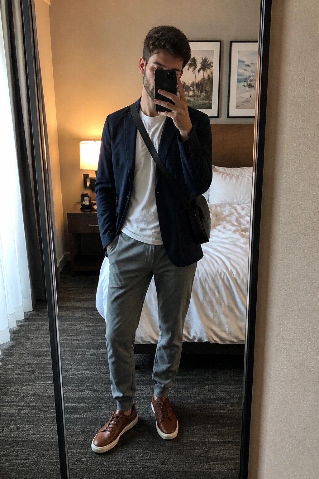 Man in navy blazer over white tee with gray pants taking hotel mirror selfie
