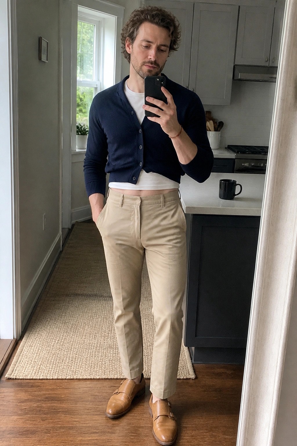 Man in navy cardigan and khaki pants taking mirror selfie in kitchen