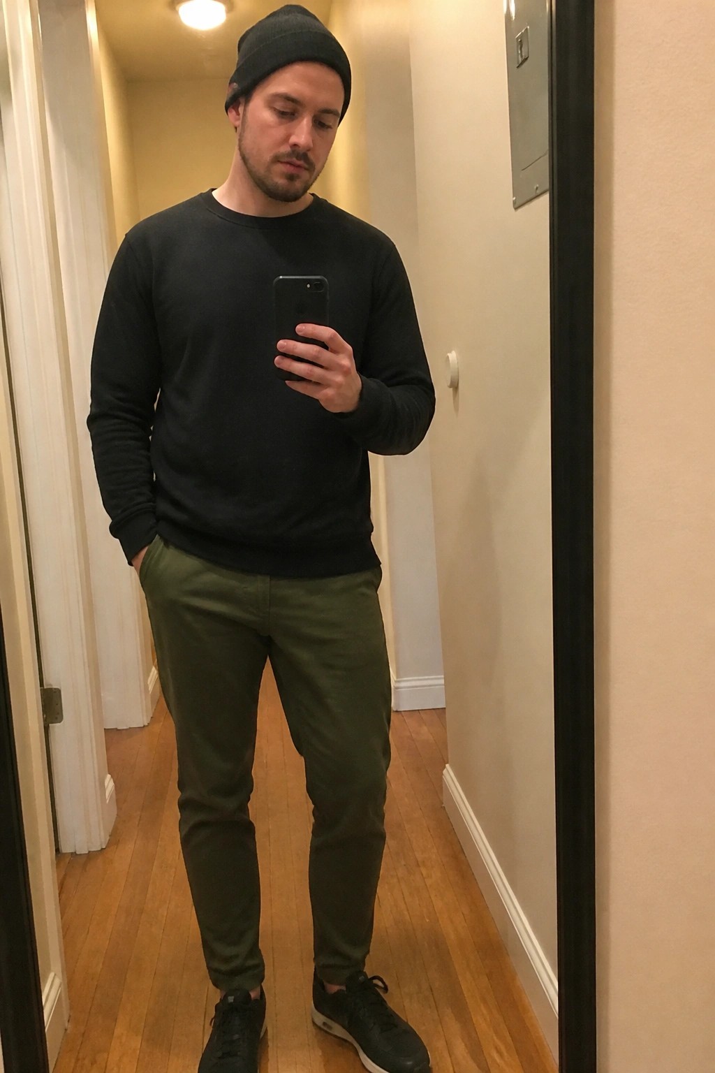 Man in black beanie and sweater with green pants taking mirror selfie