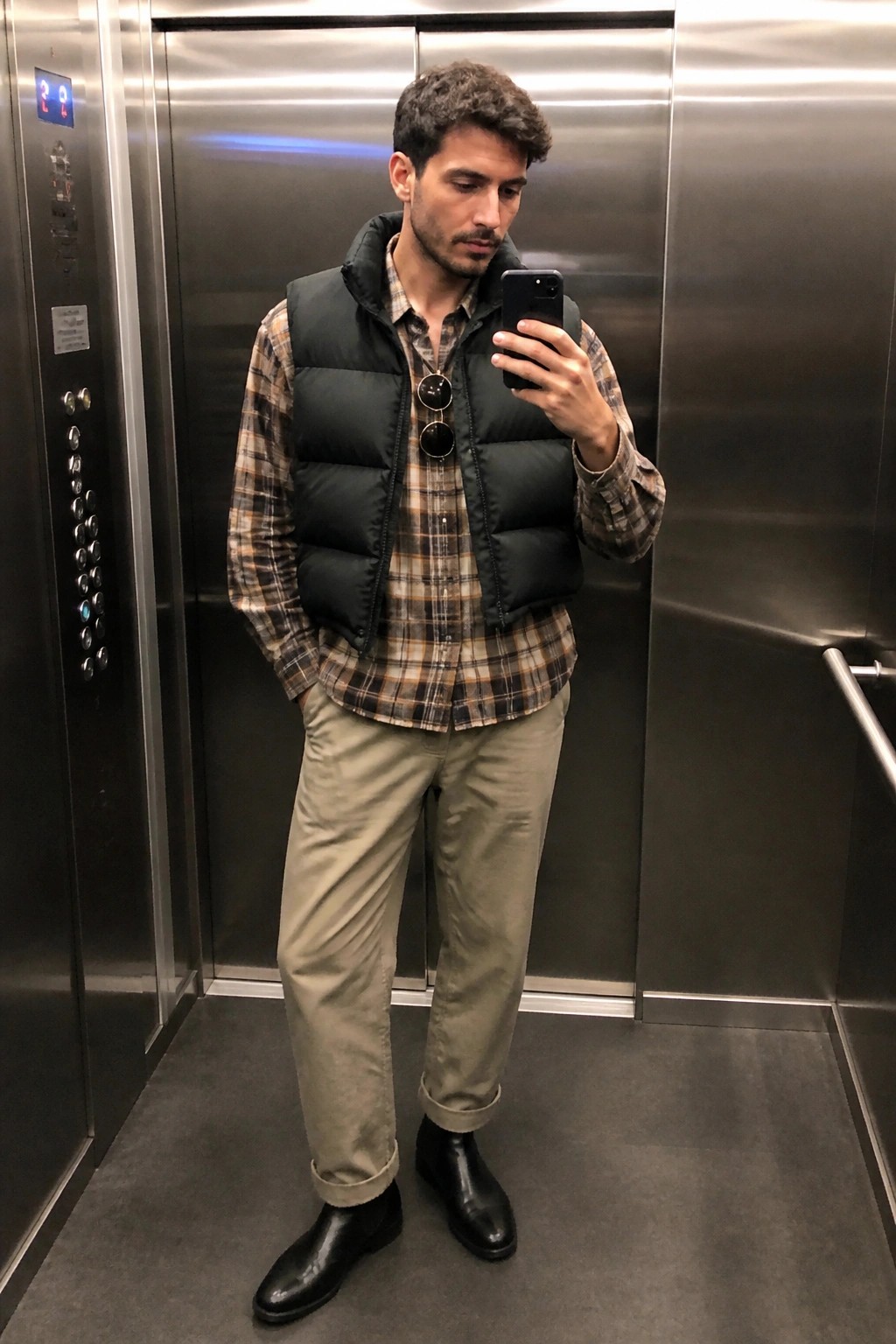 Man in black puffer vest over plaid shirt taking selfie in elevator
