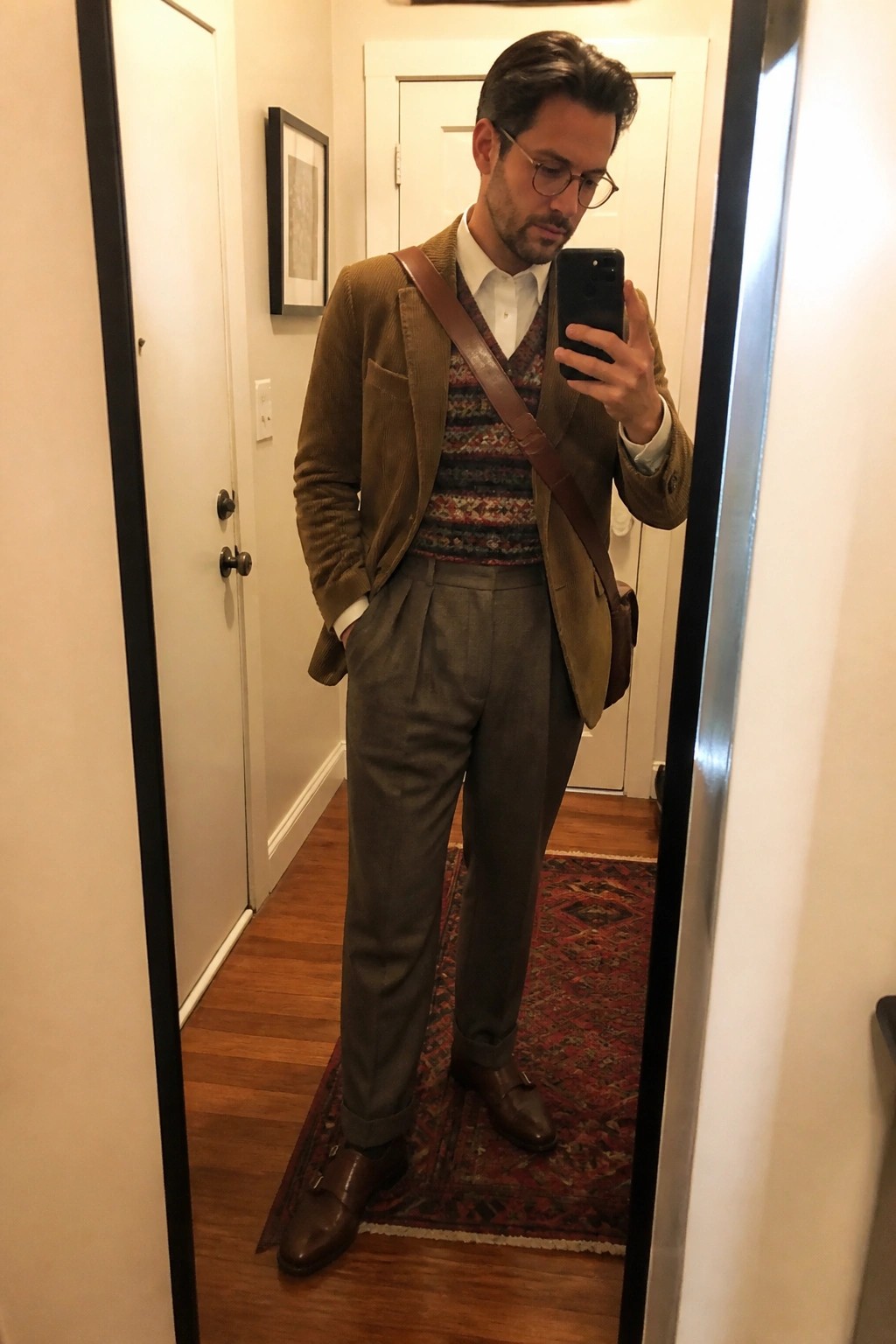Man in brown corduroy blazer and patterned sweater vest taking mirror selfie