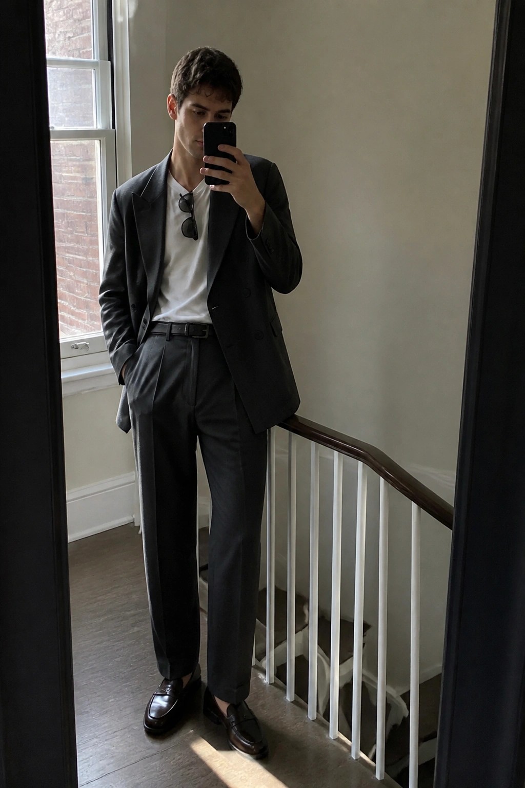 Man in dark gray suit over white t-shirt taking mirror selfie on staircase