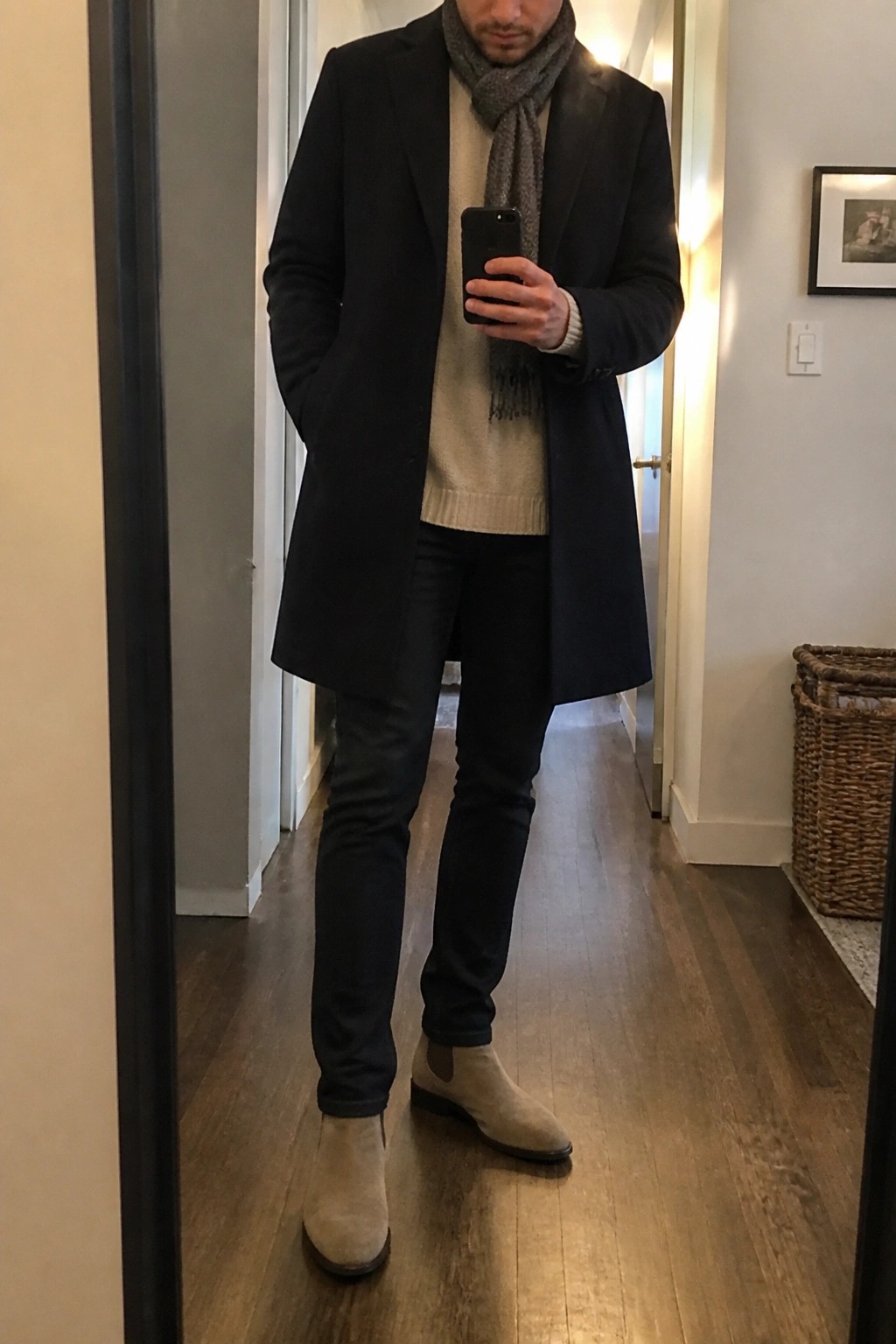 Man in navy coat, beige sweater, gray scarf, and suede boots taking mirror selfie