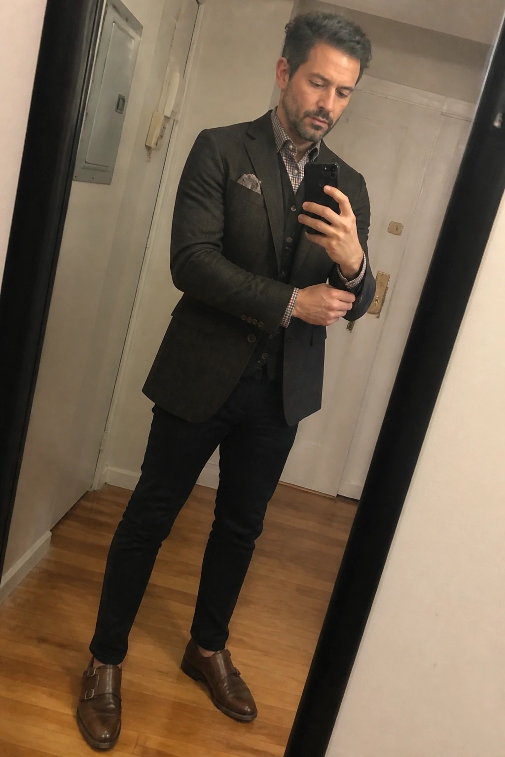 Man in dark suit and brown monk-strap shoes taking a mirror selfie with phone