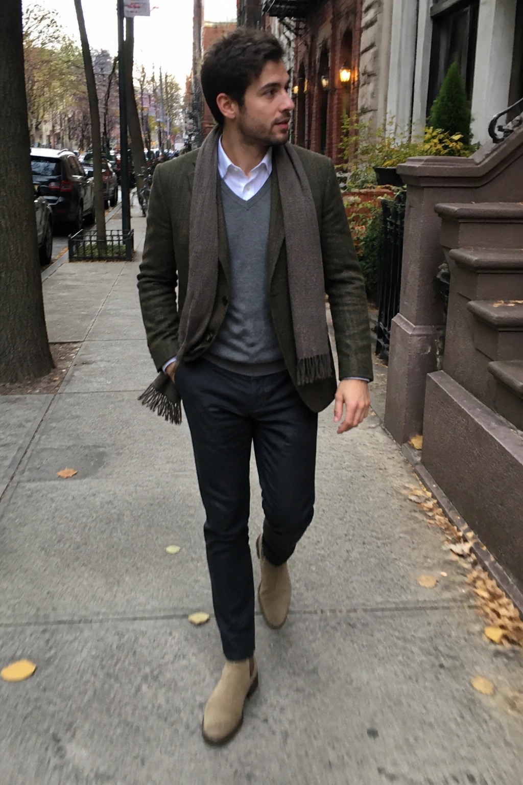 Man in olive blazer, gray sweater, and brown scarf on city sidewalk