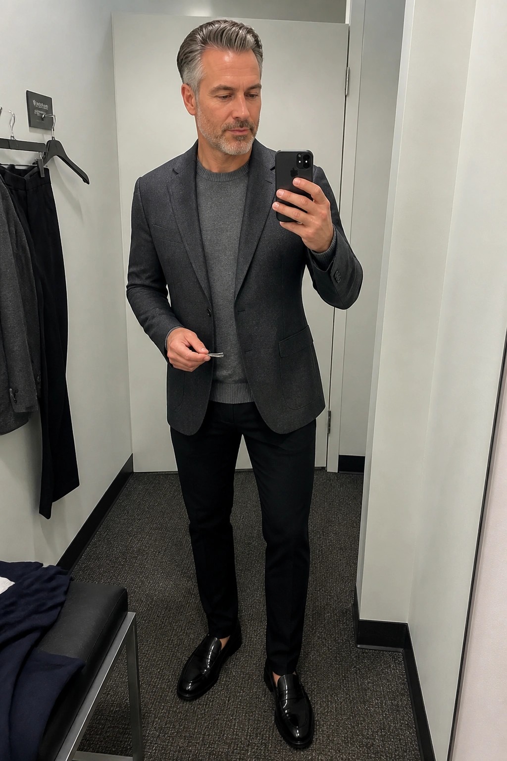 Man in gray blazer over sweater taking mirror selfie in fitting room