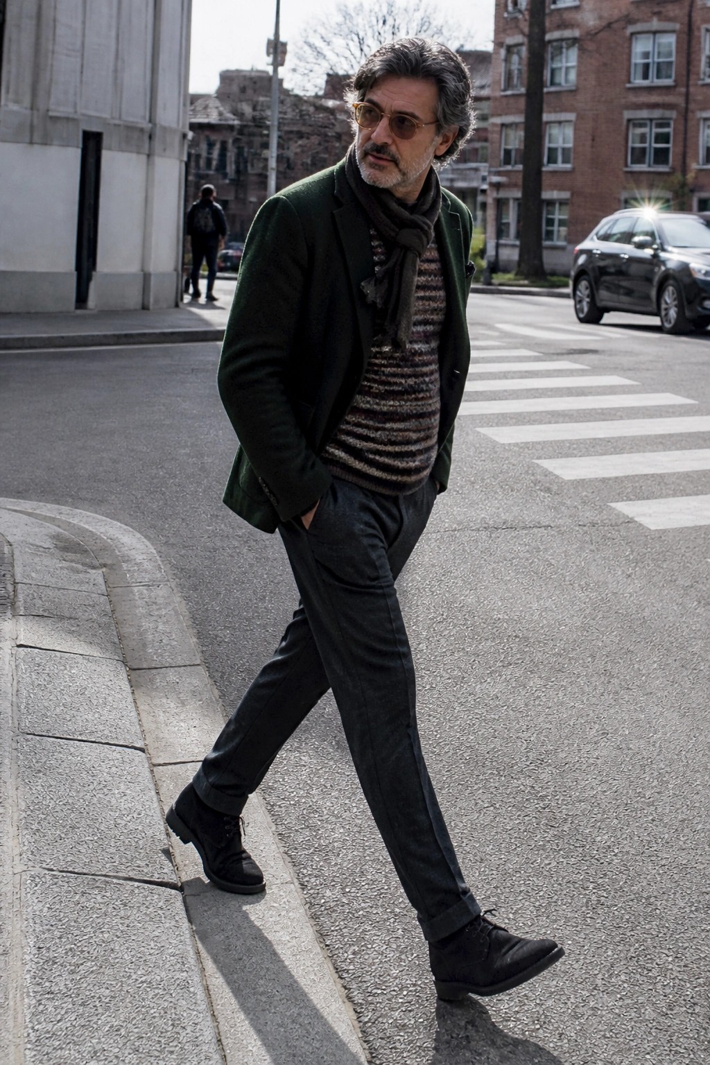 Man in green jacket and striped sweater walking on sunny city street