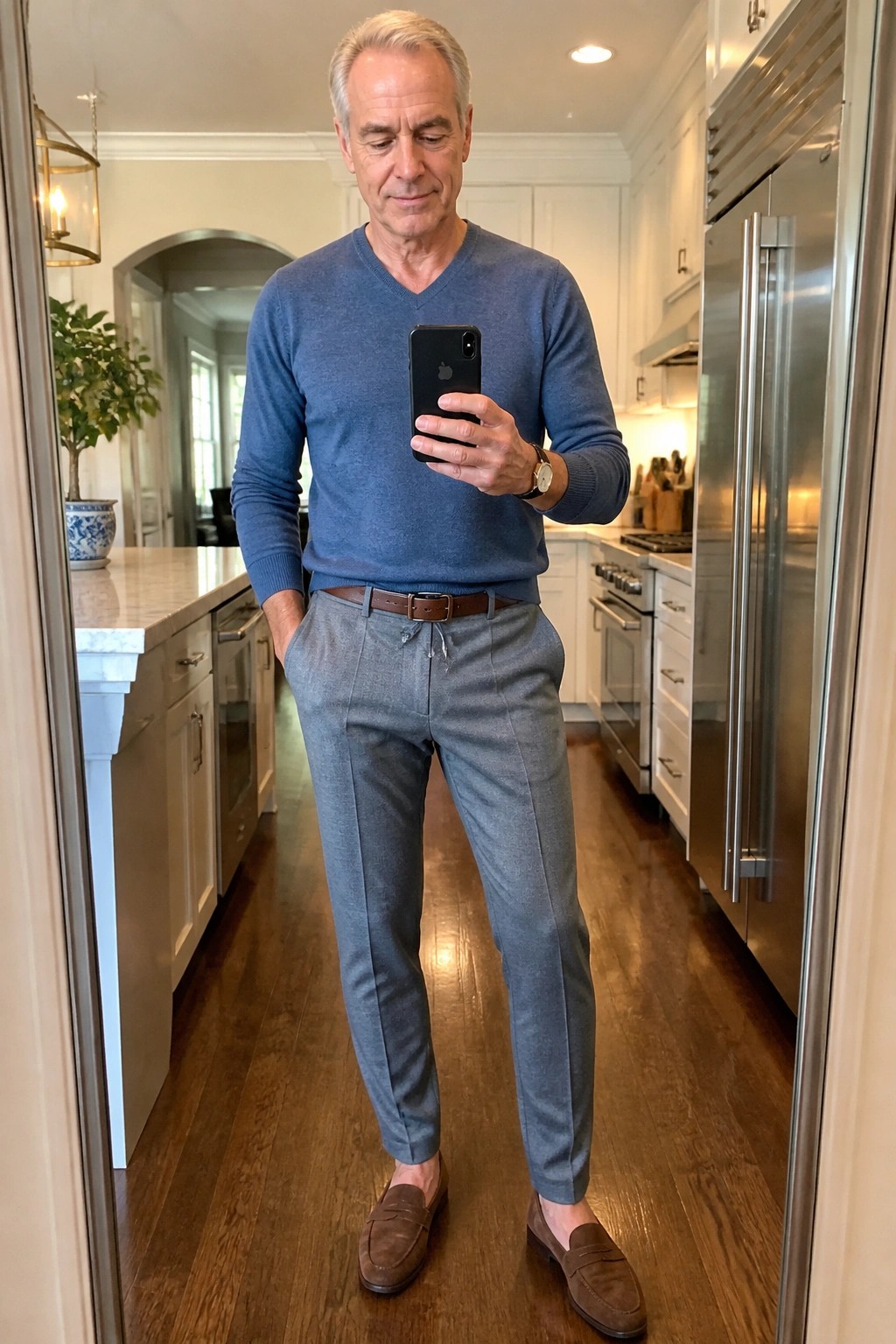 Gray-haired man in blue sweater and gray pants taking kitchen mirror selfie