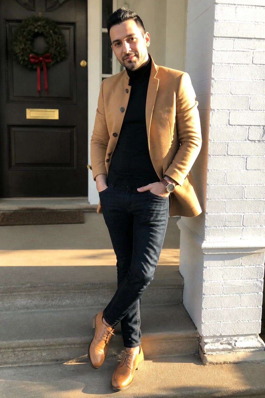 Man in tan coat over black turtleneck, dark jeans, and tan brogue shoes standing on steps.