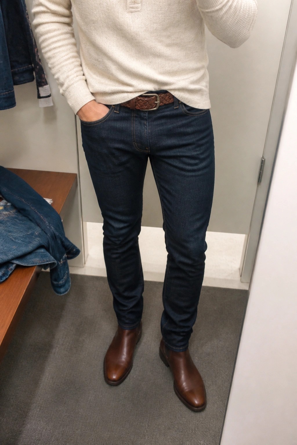 Man in cream sweater, dark jeans, brown belt and boots in fitting room