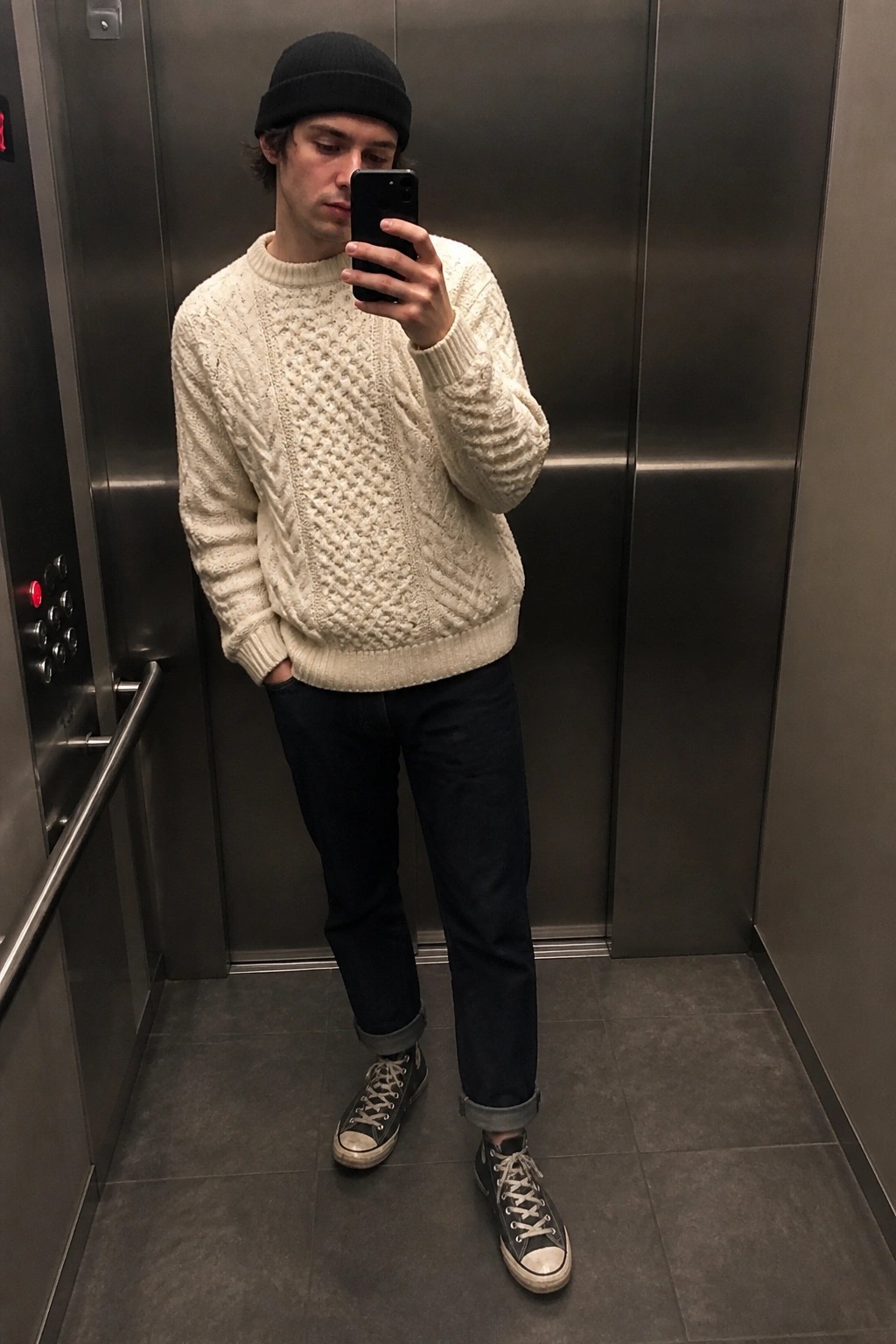 Man in cream cable-knit sweater and black beanie taking selfie in elevator