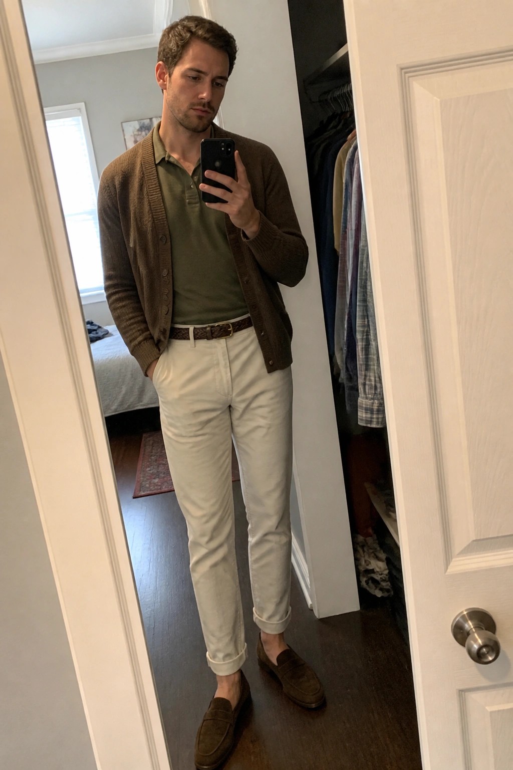 Man wearing brown cardigan over olive polo shirt with cream pants brown belt and suede loafers in mirror selfie.