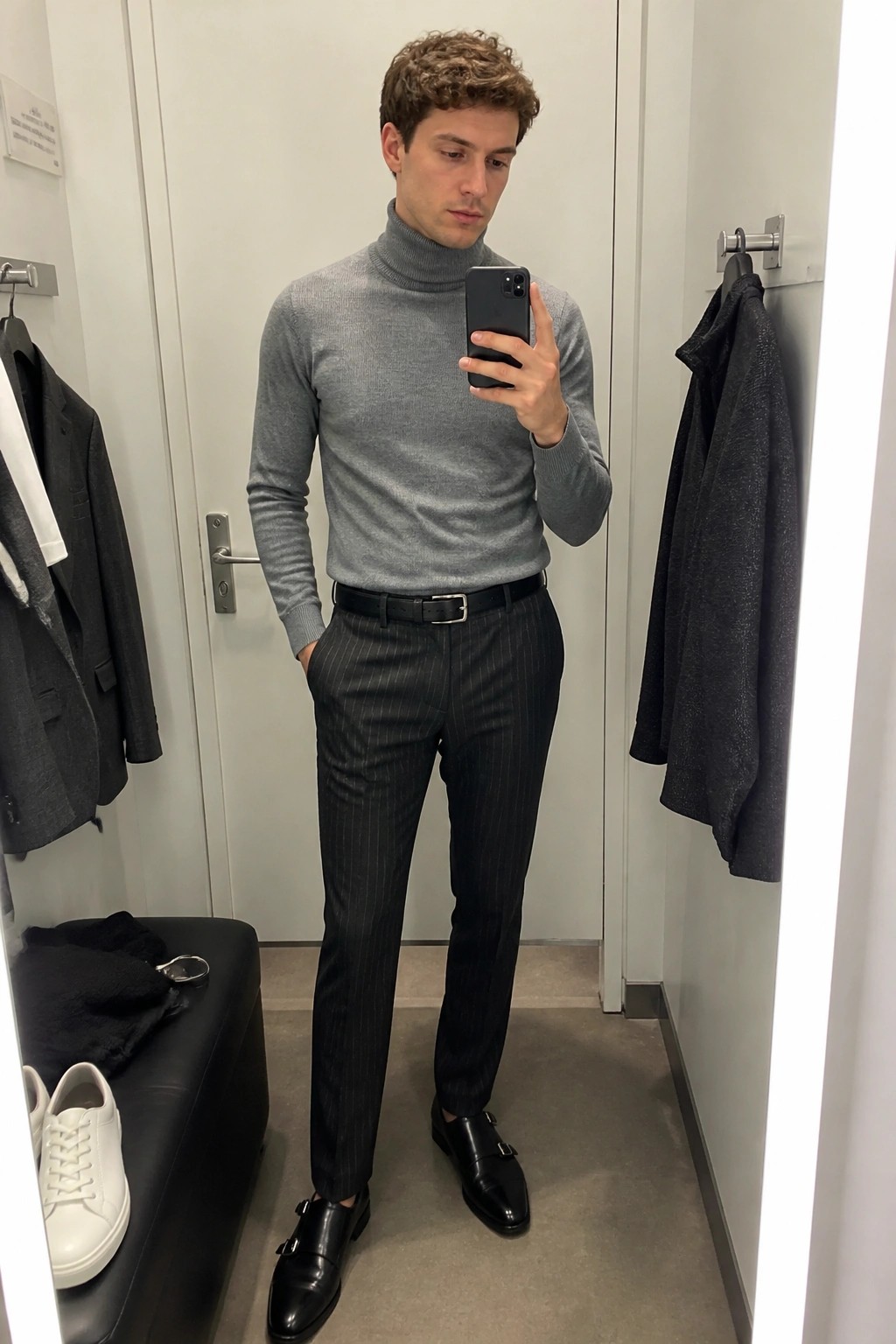 Man in gray turtleneck and pinstripe pants taking mirror selfie in fitting room