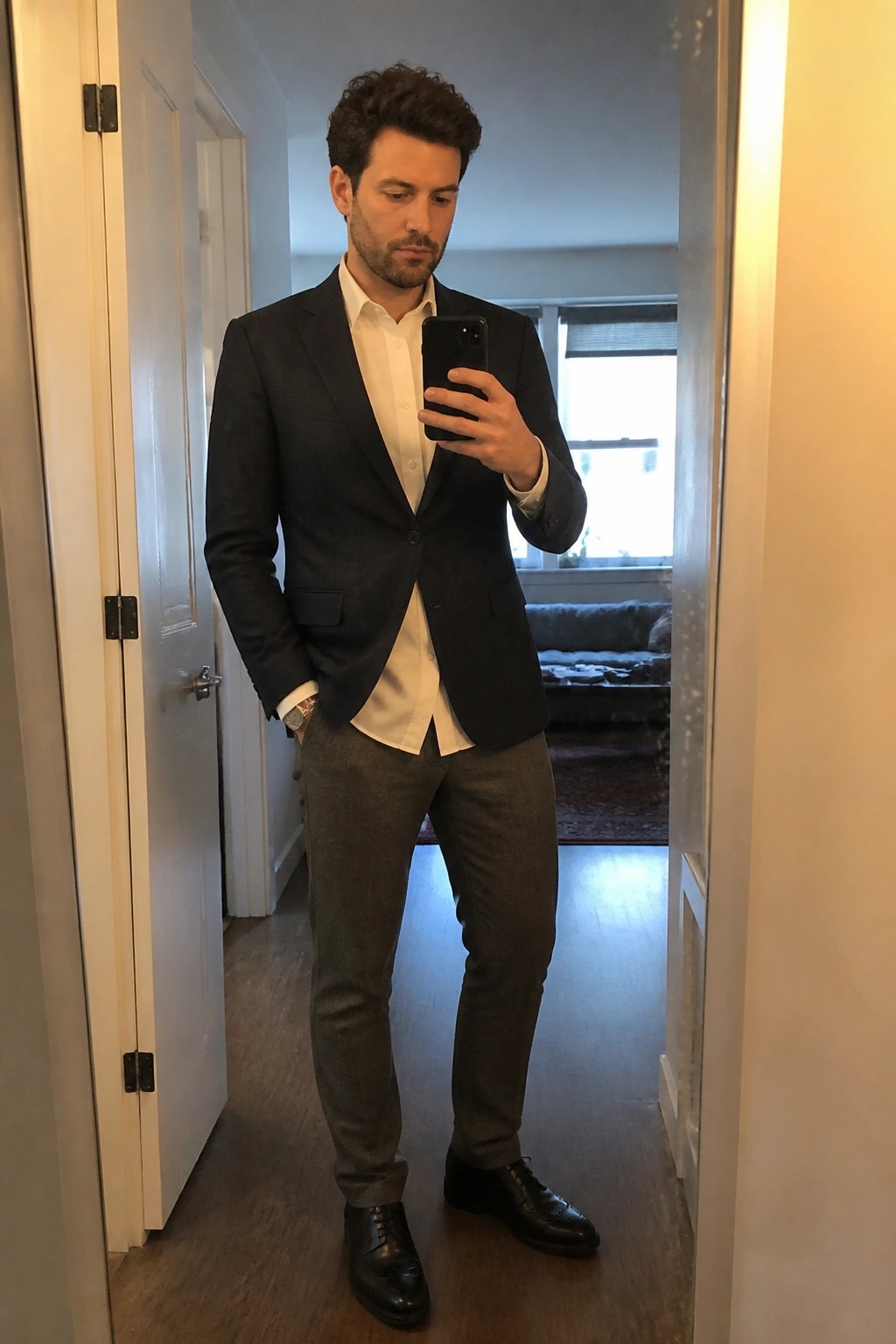 Man in navy blazer and white shirt taking mirror selfie in hallway