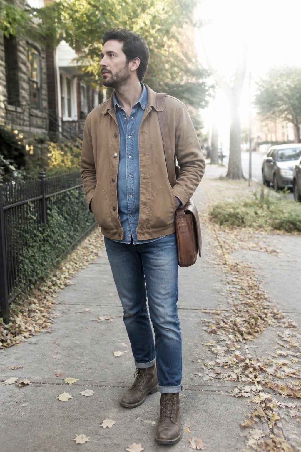 Man in brown jacket over denim shirt with leather bag on autumn sidewalk