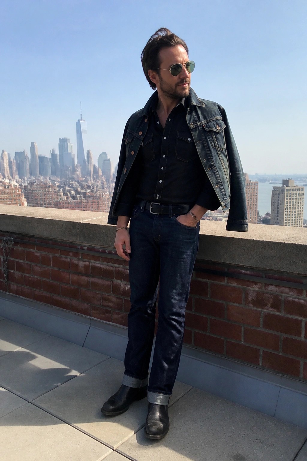 Man in denim jacket and jeans on NYC rooftop overlooking skyline