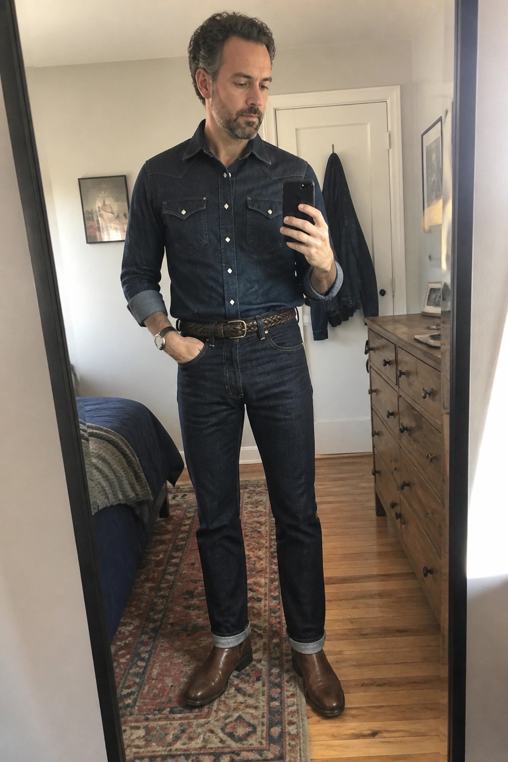 Man in denim shirt and jeans takes mirror selfie in bedroom