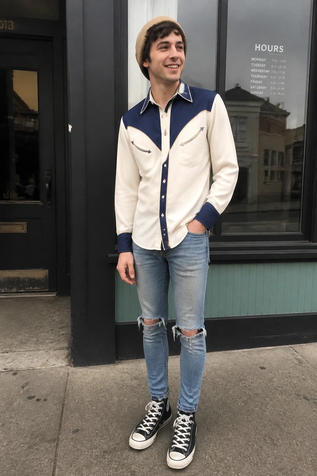 Man in beige beanie, cream-navy shirt, ripped jeans, black Converse sneakers outdoors.