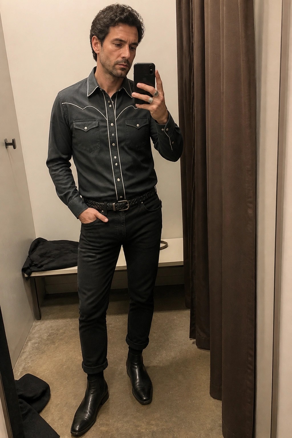 Man in black western shirt and jeans taking mirror selfie in fitting room