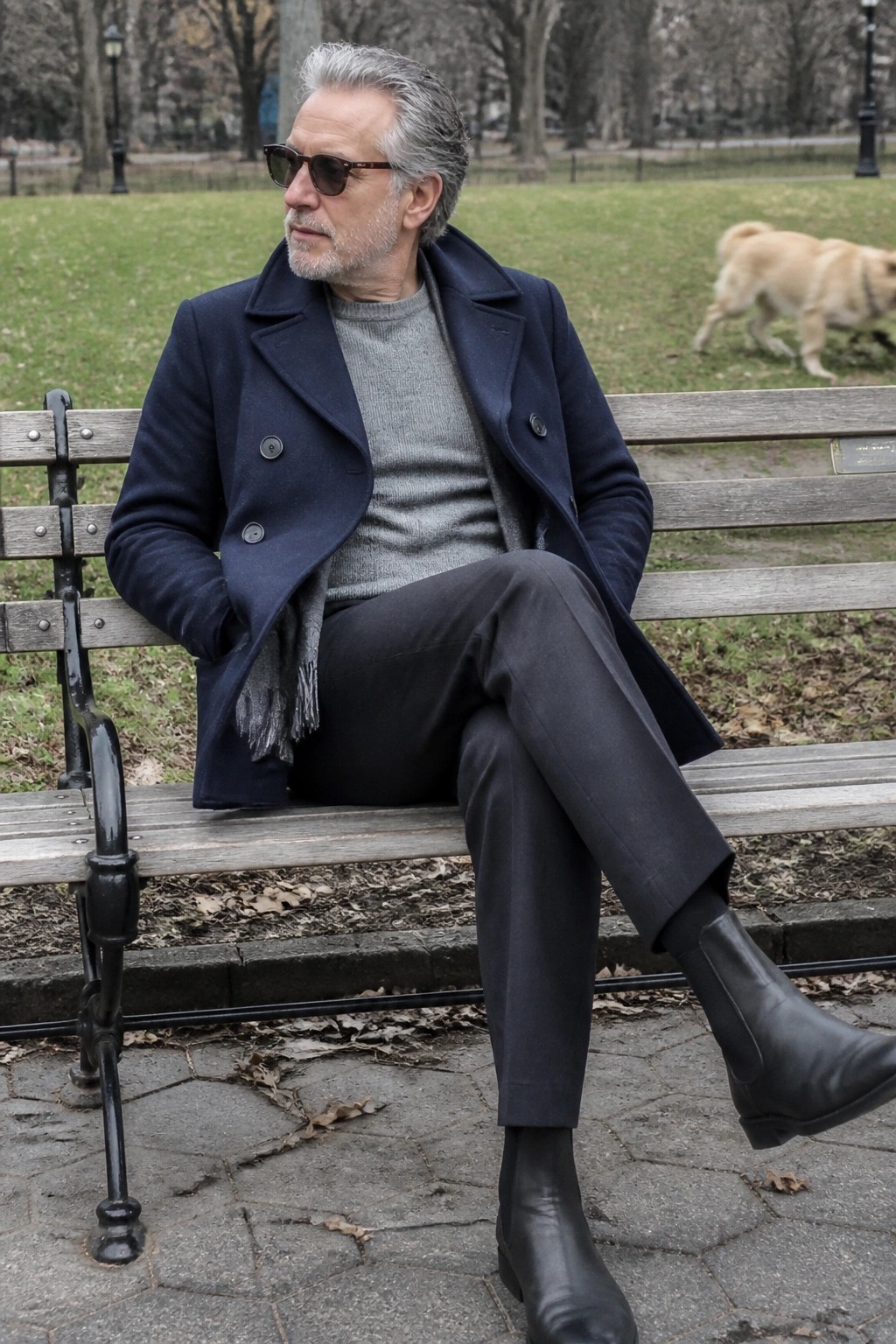 Man in navy coat and boots sits on park bench with golden retriever nearby