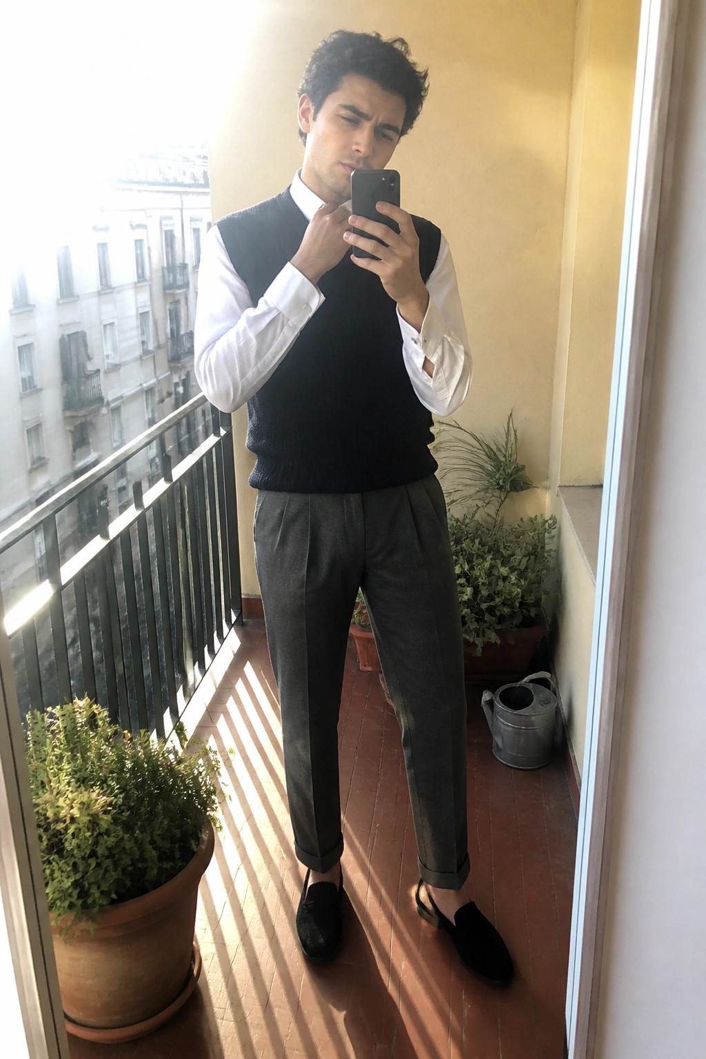 Stylish man in white shirt, black vest, and gray pants takes balcony selfie