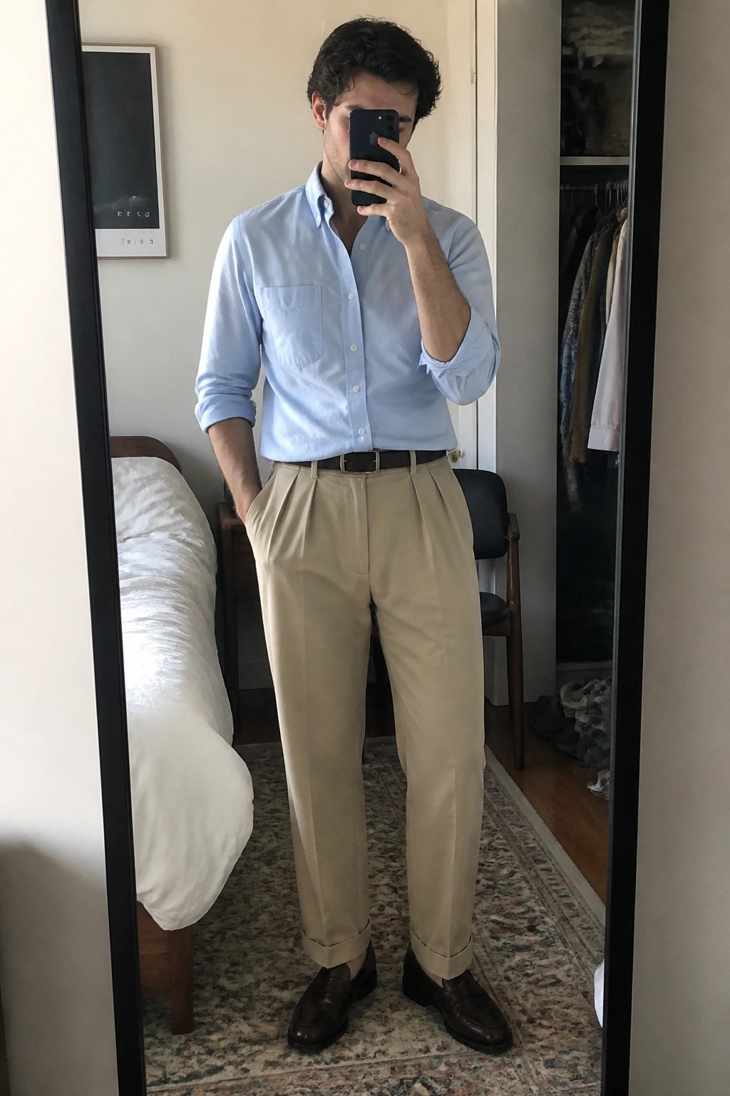 Man taking mirror selfie in light blue shirt and beige pleated trousers