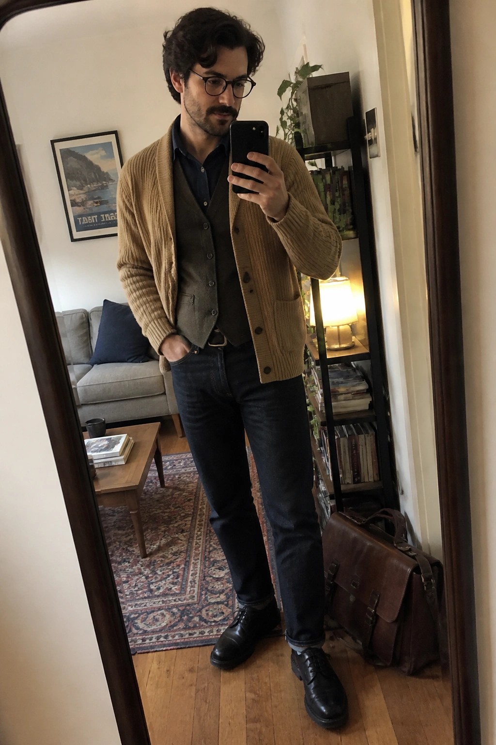 Man in tan cardigan and vest taking mirror selfie in living room