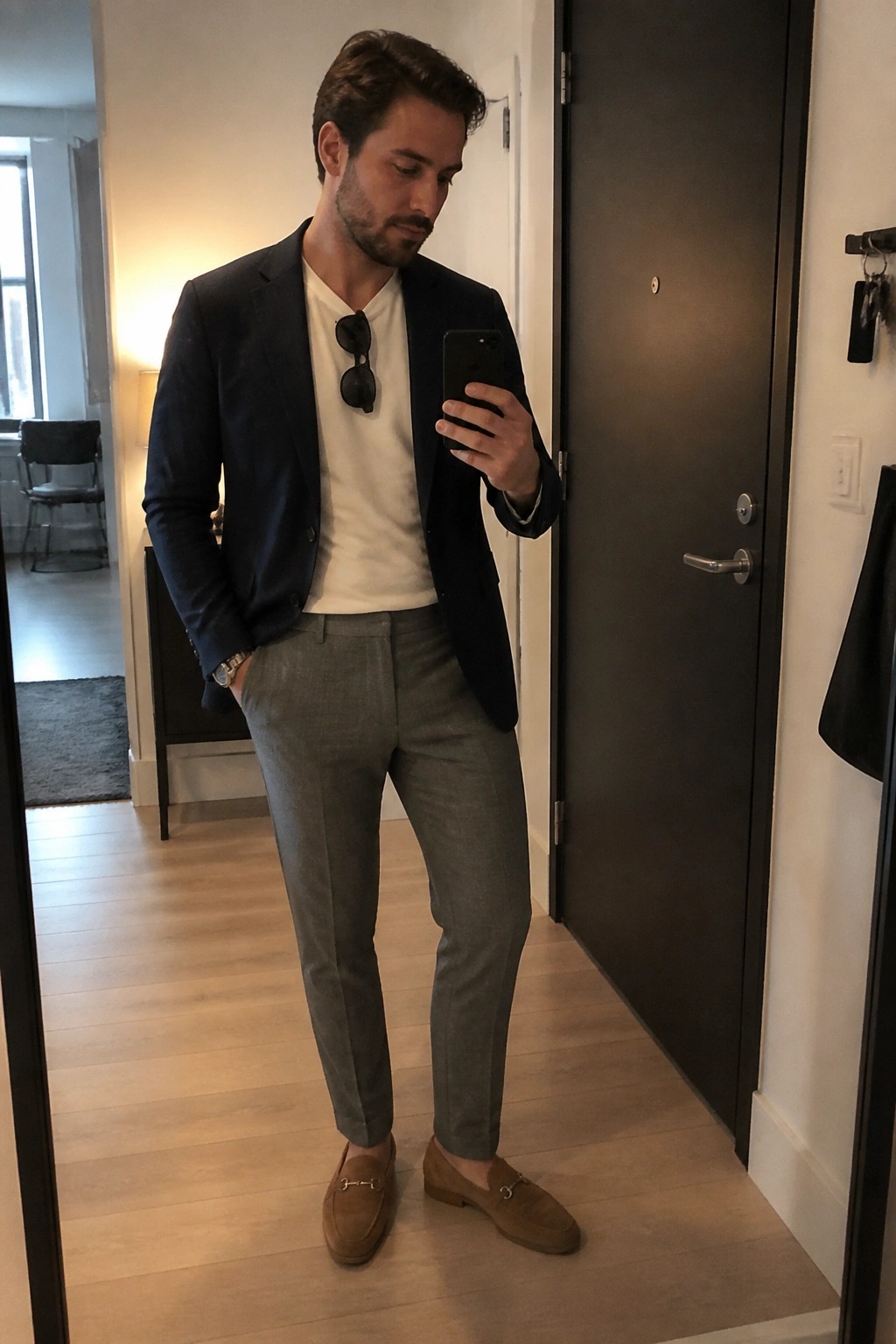 Man in navy blazer, white tee, gray trousers, and suede loafers taking mirror selfie