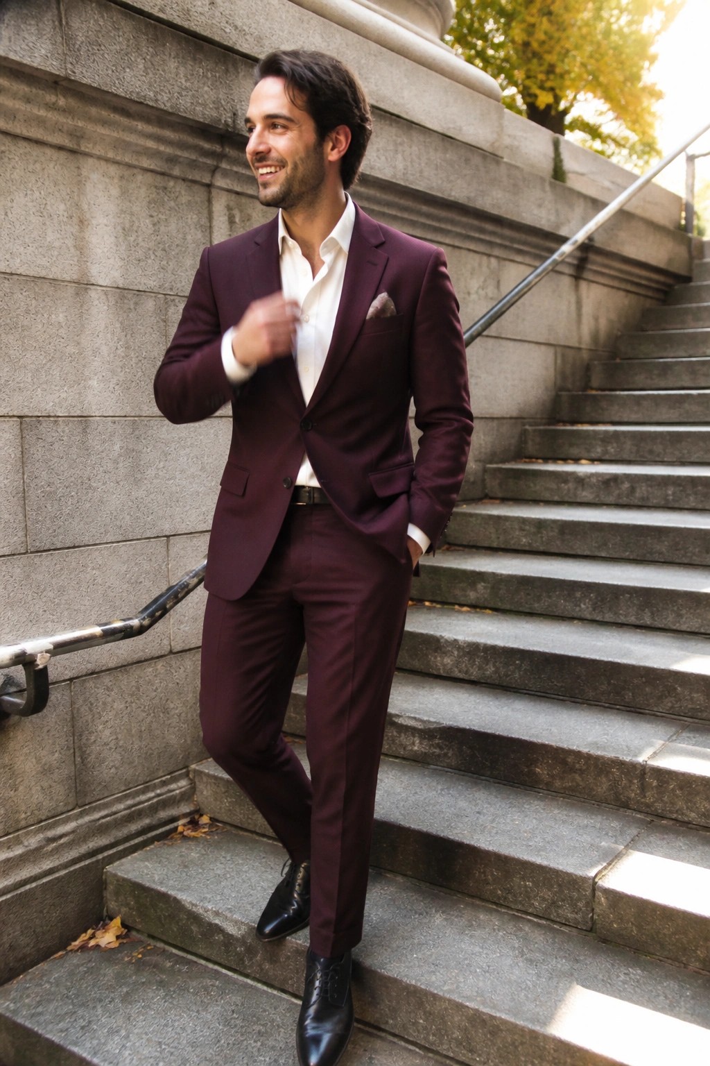 Smiling man in maroon suit stands on outdoor stone steps with hand in pocket