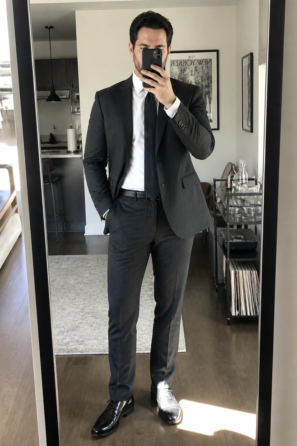 Man in dark pinstripe suit taking mirror selfie in modern apartment
