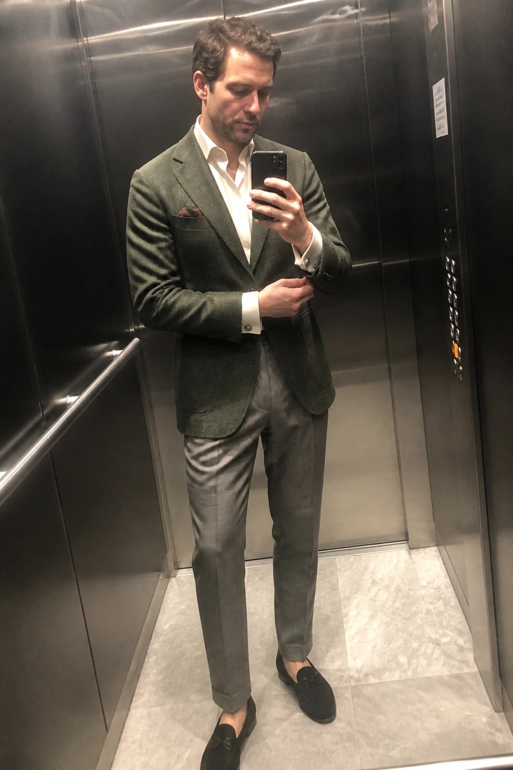 Man in green blazer taking mirror selfie while checking phone in elevator
