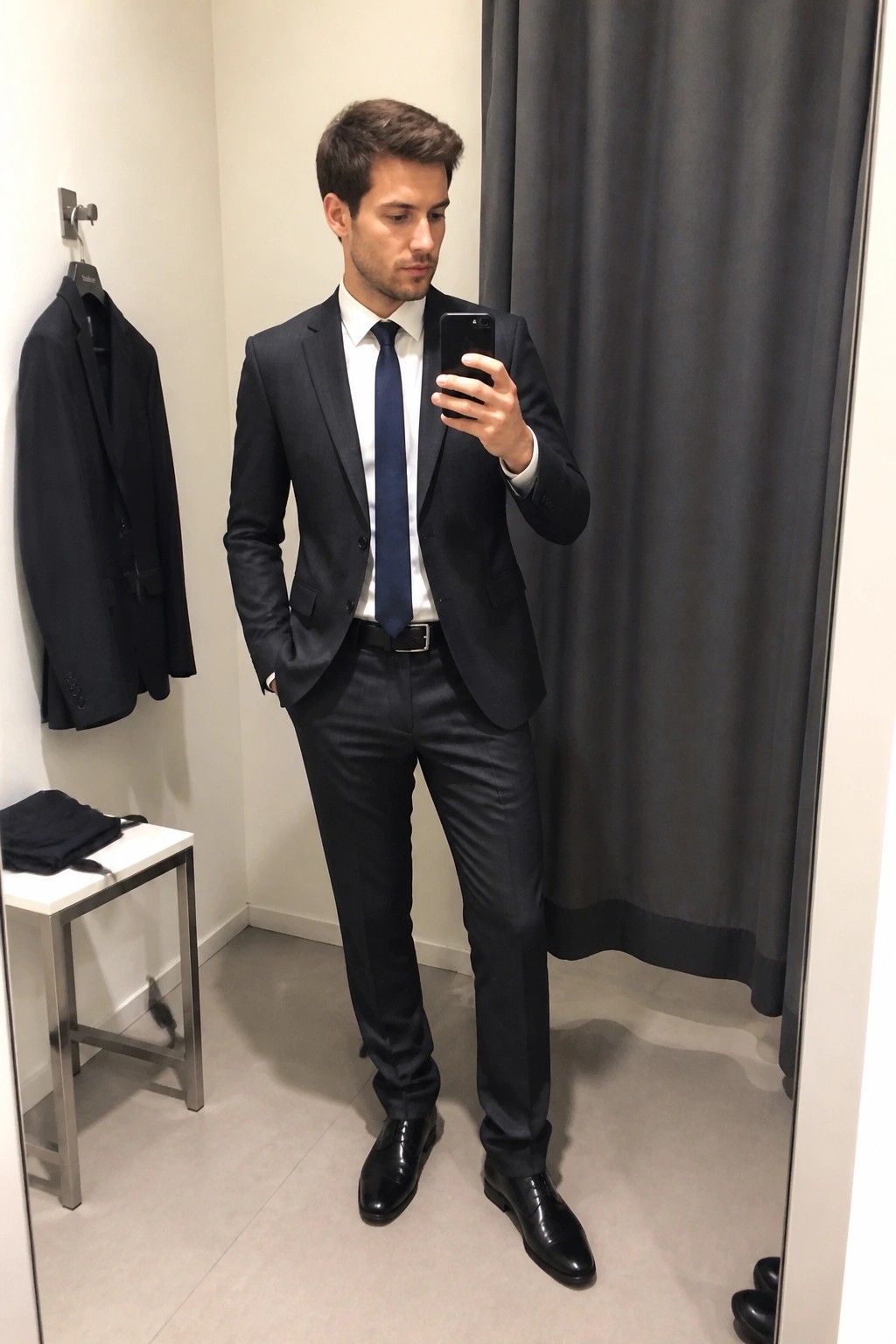 Man in dark suit and blue tie taking mirror selfie in fitting room
