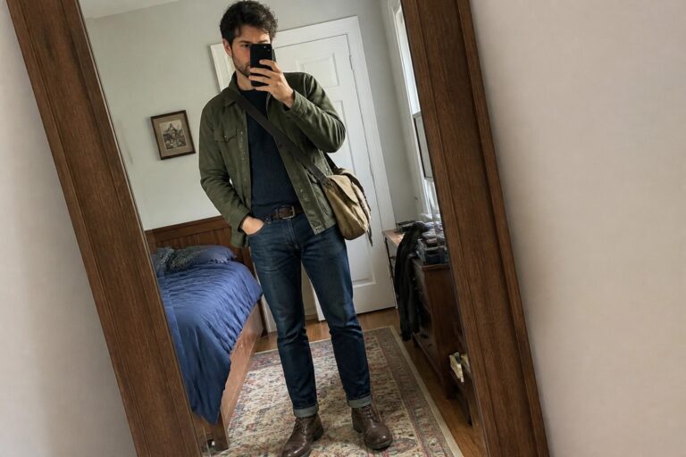 19 Rugged Workwear-Inspired Fall Outfits for Men Built Around Polished Utility Layers Man in green jacket and jeans taking mirror selfie with brown bag in bedroom
