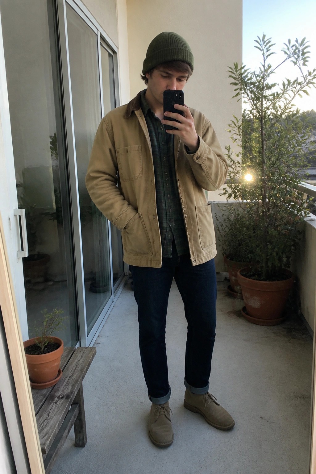 Young man in green beanie and tan jacket taking balcony selfie with phone