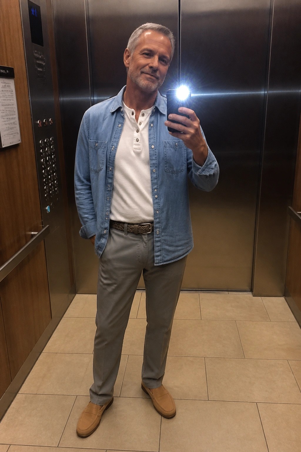 Man in blue denim shirt taking selfie with flash in elevator