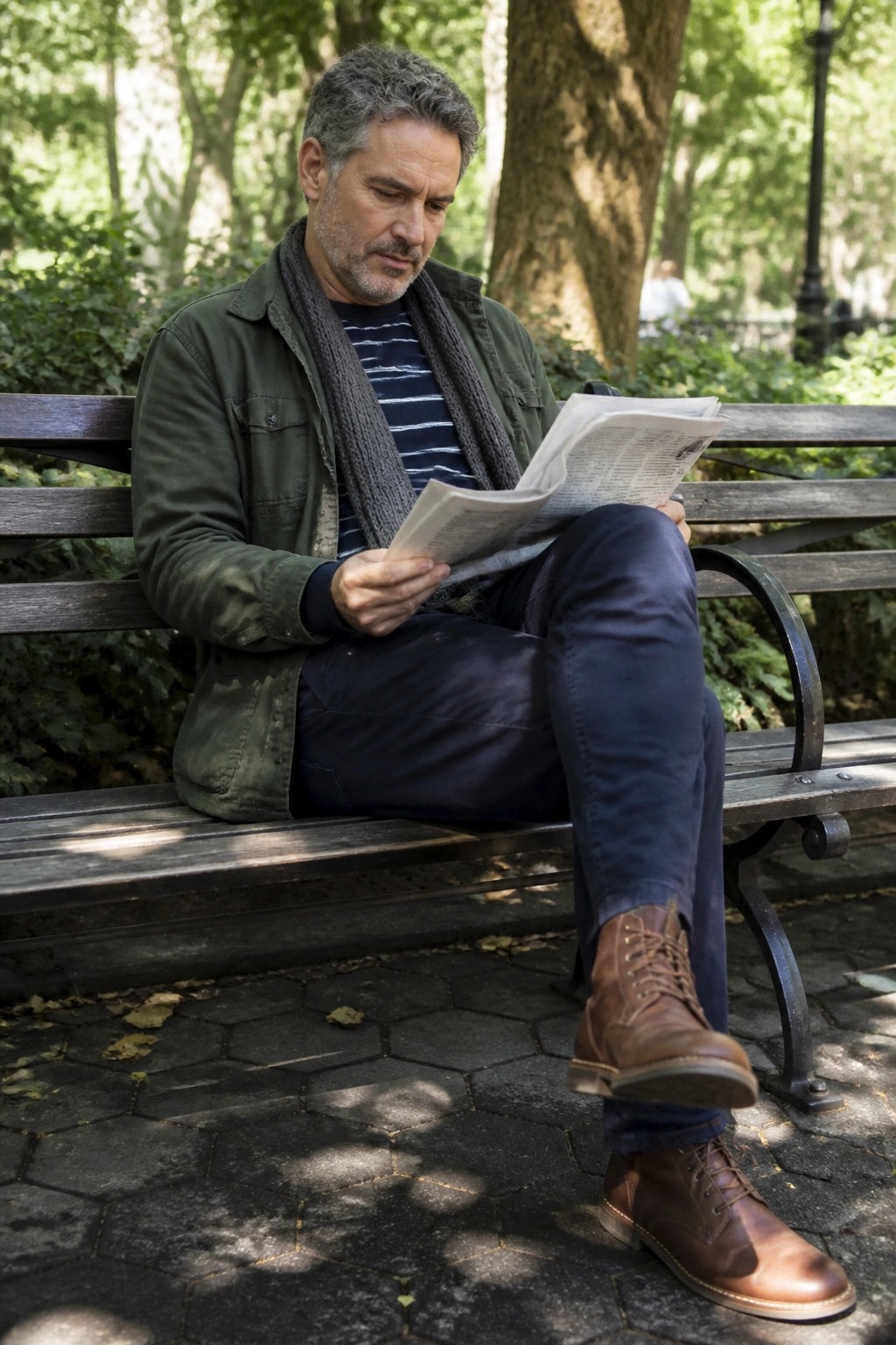 Gray-haired man reads newspaper on park bench in green jacket and brown boots