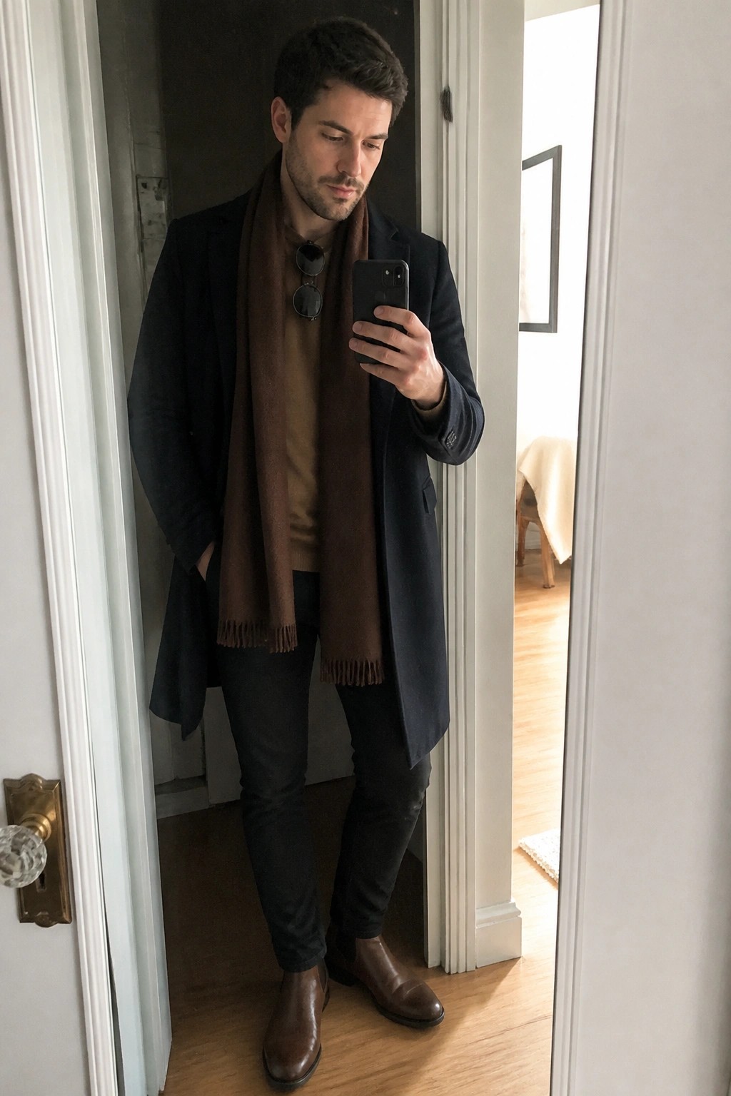 Man in navy coat and brown scarf takes mirror selfie with smartphone