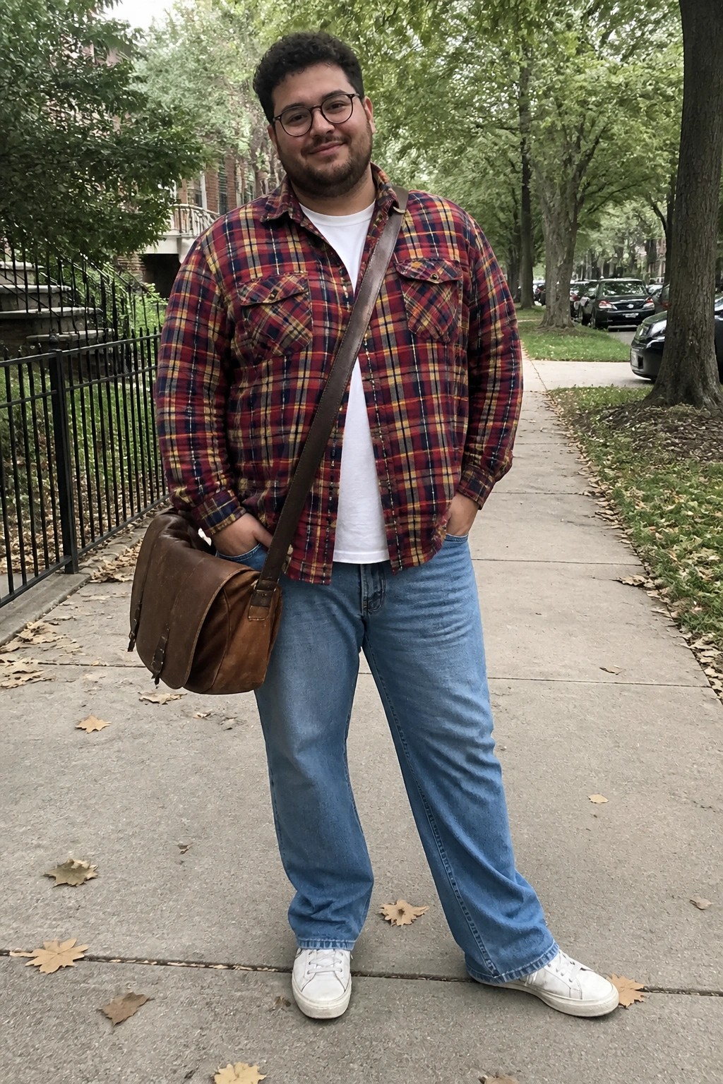 Man in red plaid shirt and jeans with brown messenger bag on sidewalk.