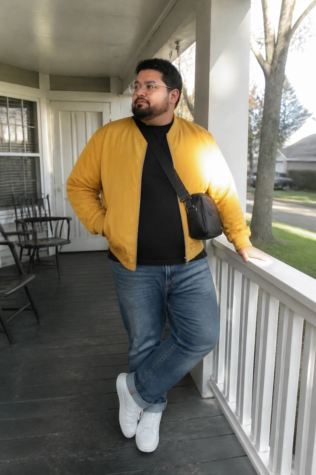 Man in yellow bomber jacket with black crossbody bag on wooden porch