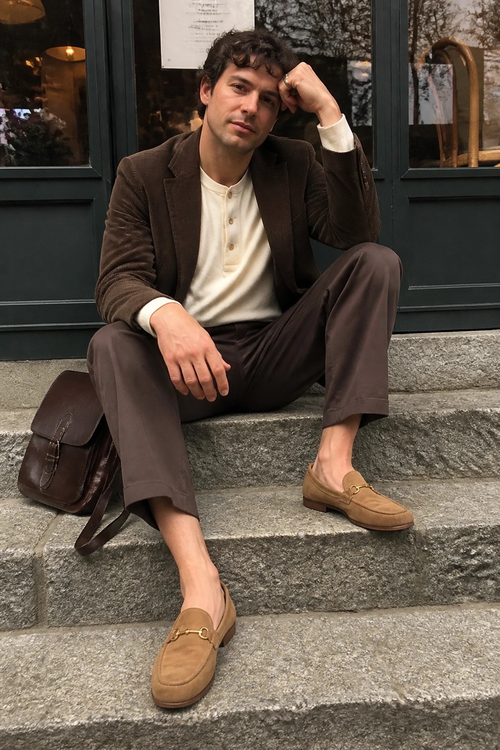 Man in brown corduroy blazer and suede loafers on stone steps with leather bag