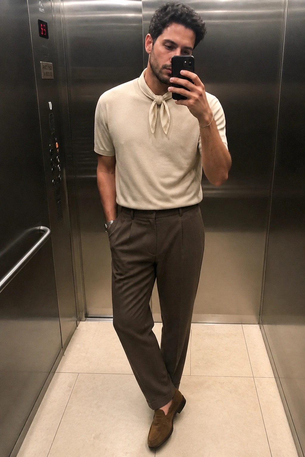 Man in beige knotted shirt and brown pants taking selfie in elevator