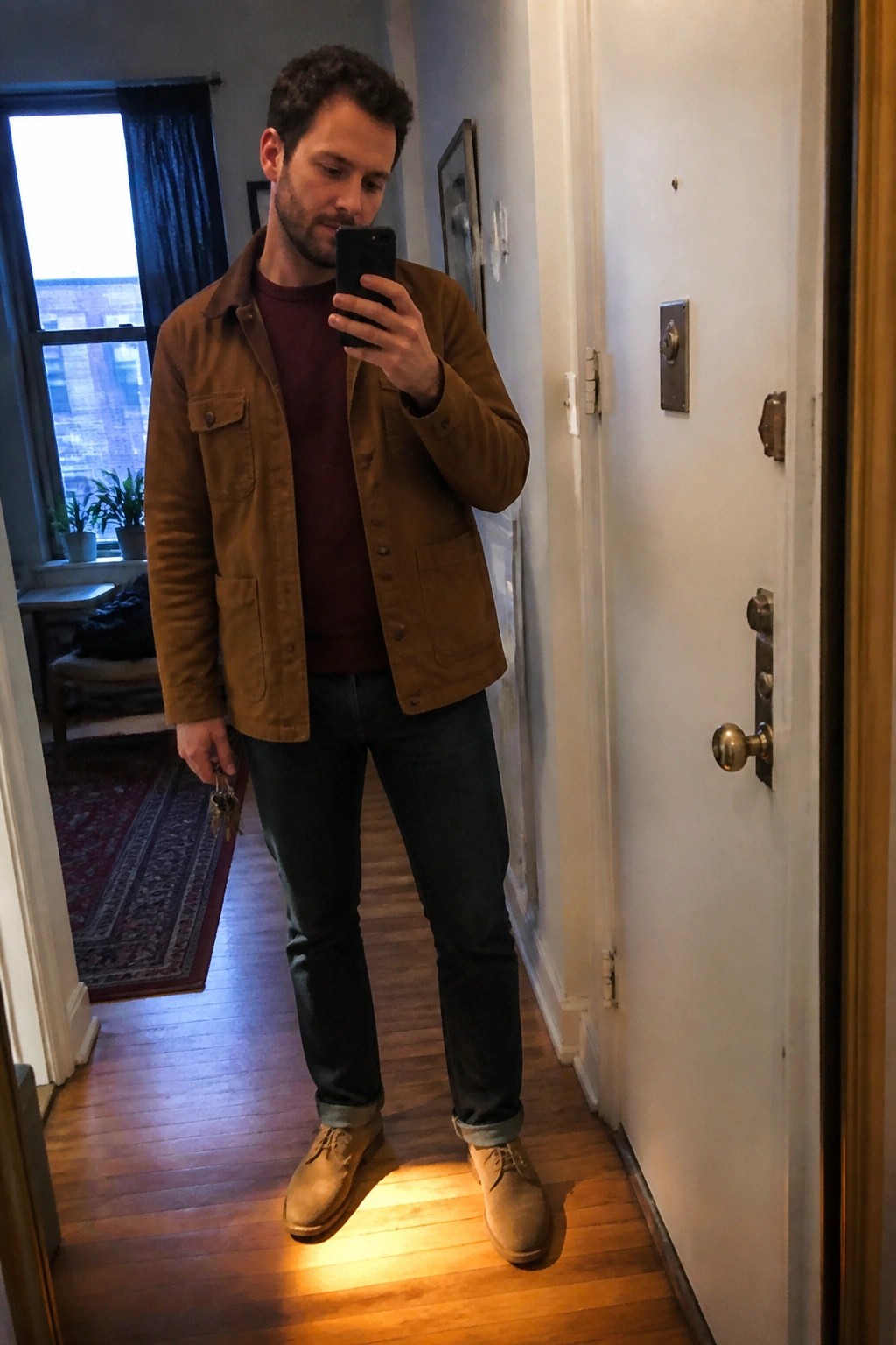 Man in brown jacket over maroon shirt taking mirror selfie while holding keys