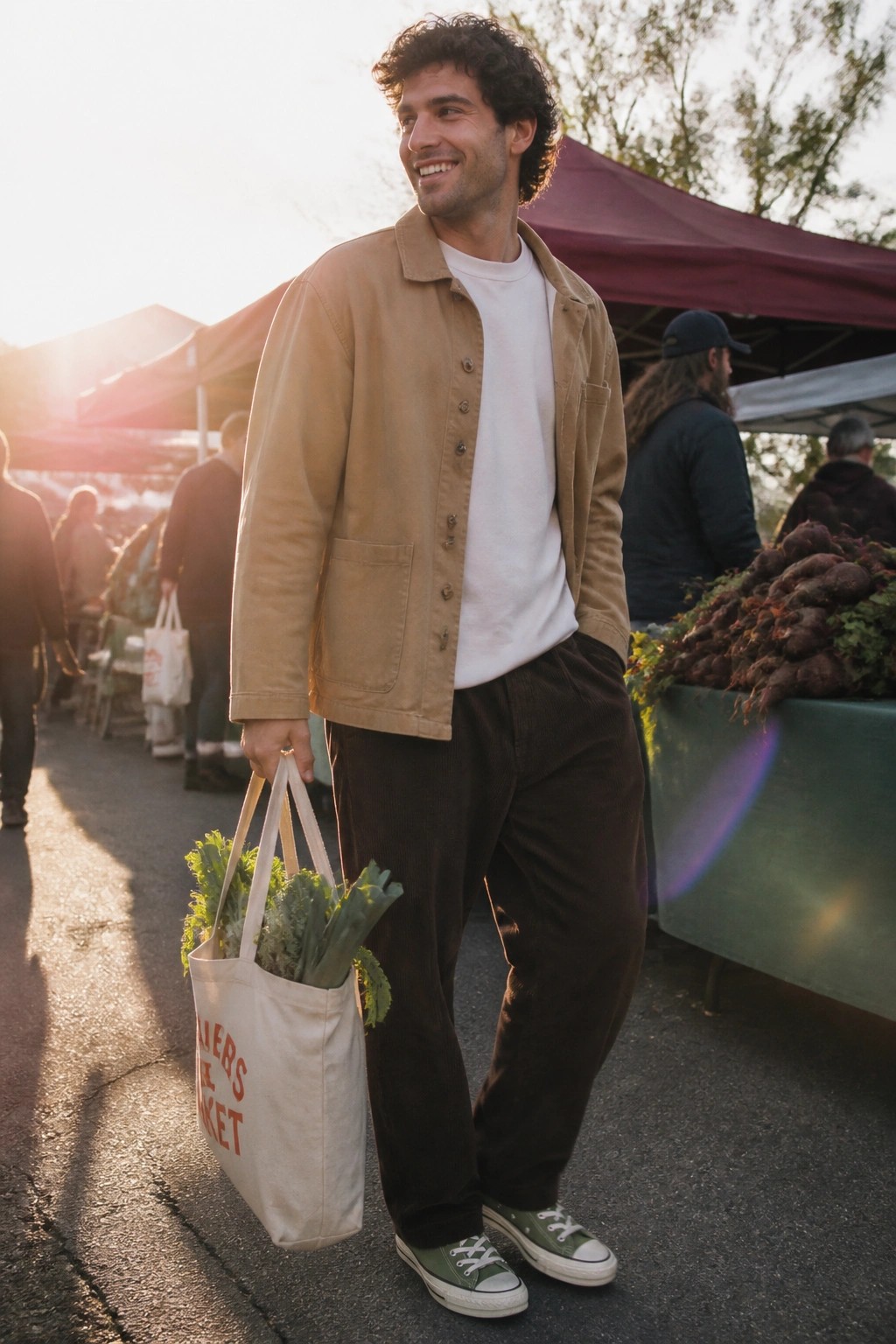Man in tan jacket carries vegetable-filled tote bag at sunny farmers market.