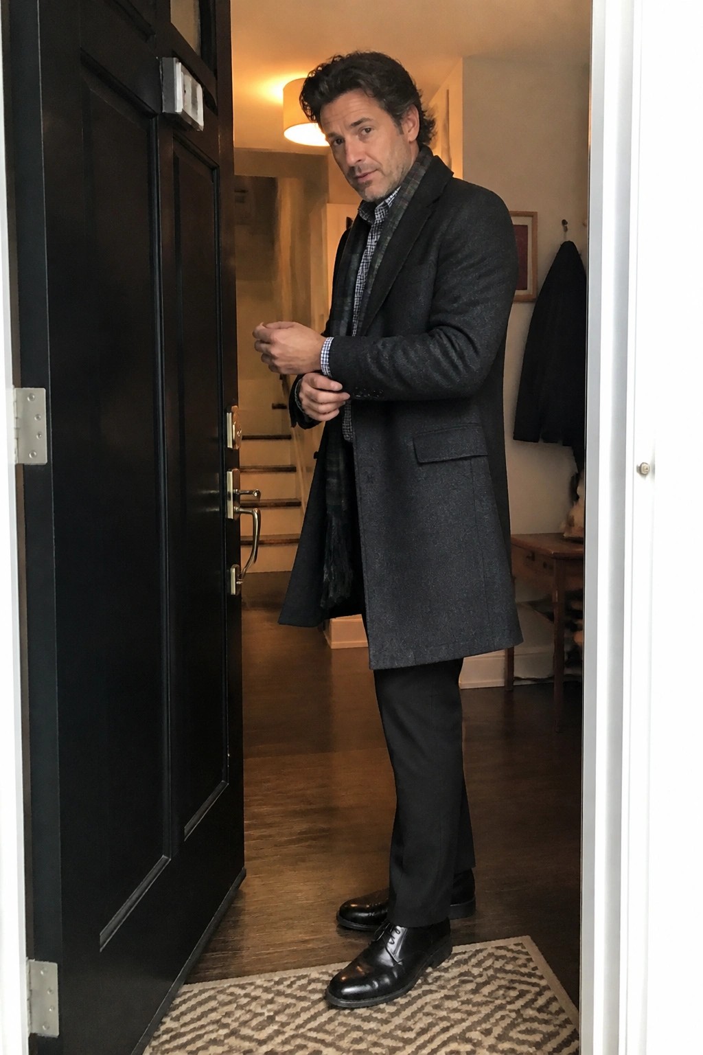 Man in dark overcoat adjusting cuffs while standing in open doorway