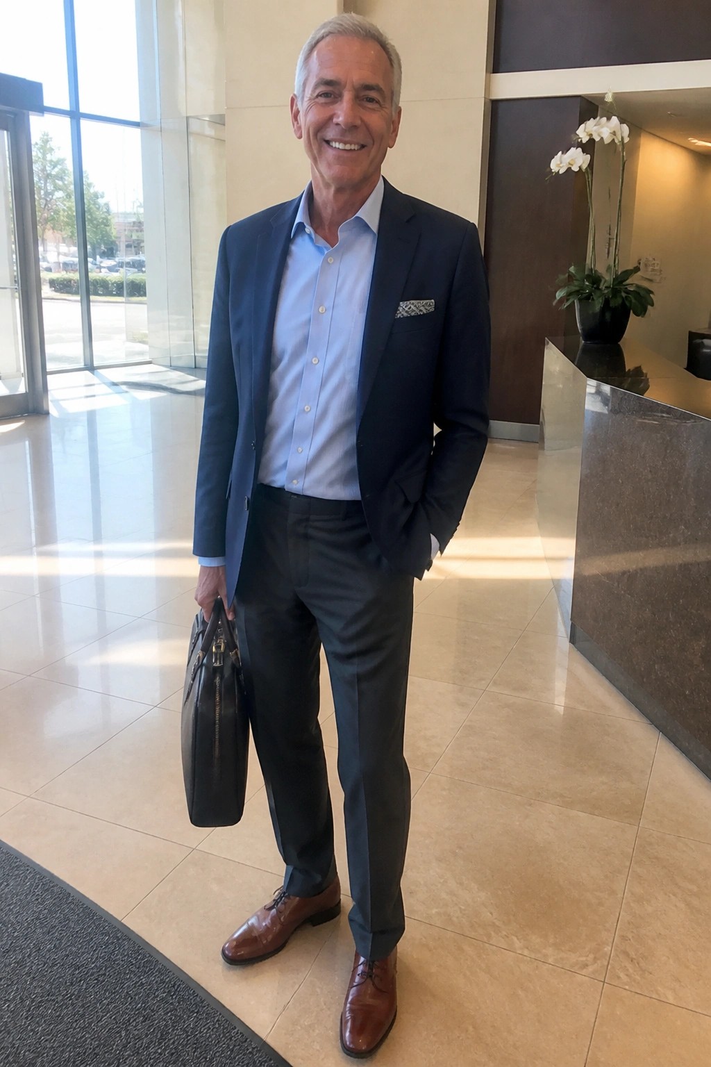 Smiling gray-haired man in navy blazer holds briefcase in modern lobby.