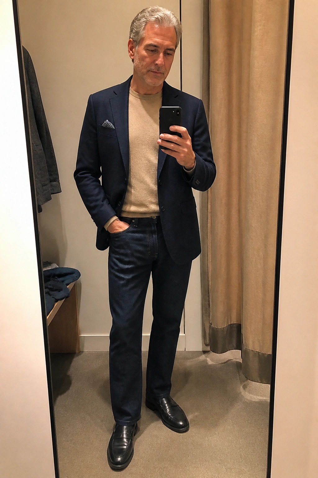 Gray-haired man in navy blazer over beige sweater taking mirror selfie with phone