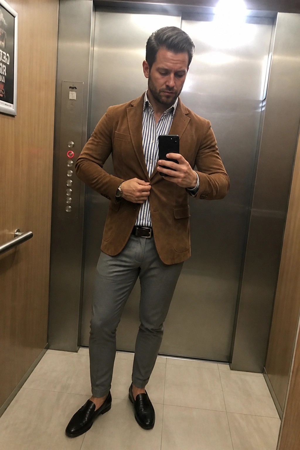 Man in brown suede blazer adjusts jacket while holding phone in elevator