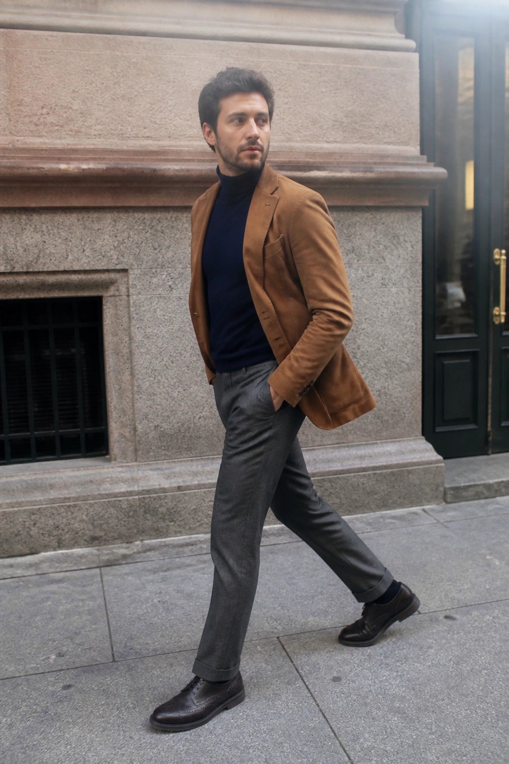 Man in brown suede blazer over navy turtleneck walking on city sidewalk